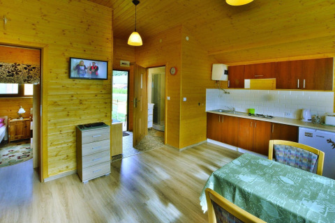 Interior of a cozy wooden cabin with kitchen, dining table, bedroom, and TV at Domki letniskowe Rusinowo, Denmark.