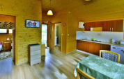 Interior of a cozy wooden cabin with kitchen, dining table, bedroom, and TV at Domki letniskowe Rusinowo, Denmark.