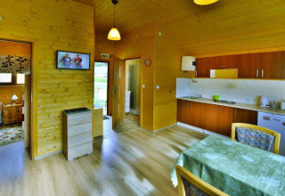 Interior of a cozy wooden cabin with kitchen, dining table, bedroom, and TV at Domki letniskowe Rusinowo, Denmark.