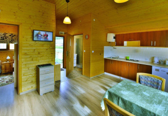 Interior de una acogedora cabaña de madera con cocina, mesa de comedor, dormitorio y televisor en Domki letniskowe Rusinowo.