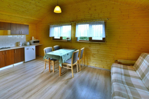Cozy wooden cabin interior with a dining table, kitchenette, and sofa at Domki letniskowe Rusinowo in Denmark.