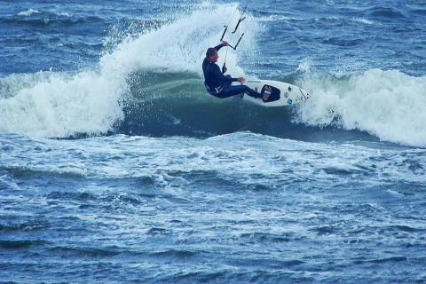 Kitesurfer riding a wave near Domki letniskowe Rusinowo, impressive action at the seaside in Denmark.