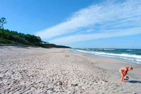 Photo of a quiet sandy beach near Domki letniskowe Rusinowo, with a girl playing with a ball by the sea.