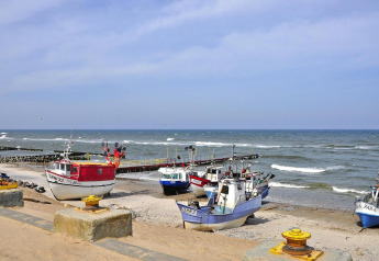 Des bateaux de pêche reposent sur une plage de sable près de la mer avec jetée et ciel bleu.