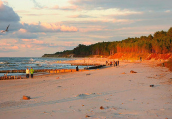 Solnedgang på en fredelig sandstrand nær Domki letniskowe Rusinowo med mennesker, hav og skov.