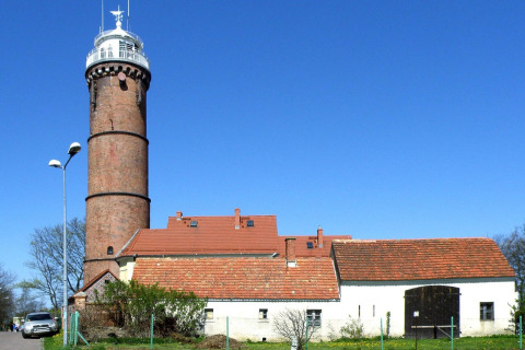 Brick building with red roof and lighthouse under a clear blue sky at Domki letniskowe Rusinowo.