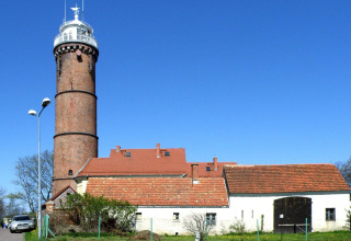 Brick building with red roof and lighthouse under a clear blue sky at Domki letniskowe Rusinowo.