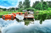 Chalets au bord d'un lac avec pédalos et barque, entourés de verdure et d'un ponton en bois paisible.