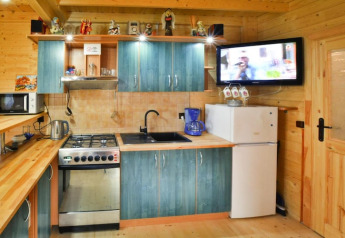 Gezellige chaletkeuken met blauwe kasten, fornuis, koelkast, microgolfoven en TV aan de muur.