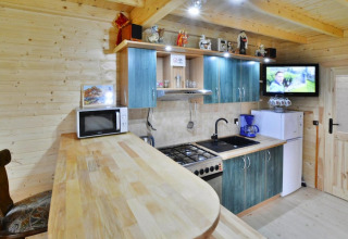 Moderne Küchenzeile in einer Holzhütte mit blauen Schränken, Herd, Mikrowelle, Kühlschrank und Fernseher.