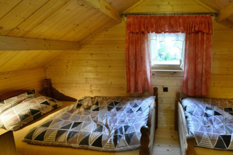 Gemütliches Schlafzimmer mit zwei Einzelbetten, Holzwänden und einem kleinen Fenster im Holzhaus PATRYK.