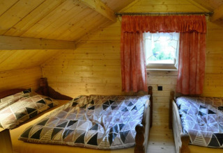 Gemütliches Schlafzimmer mit zwei Einzelbetten, Holzwänden und einem kleinen Fenster im Holzhaus PATRYK.