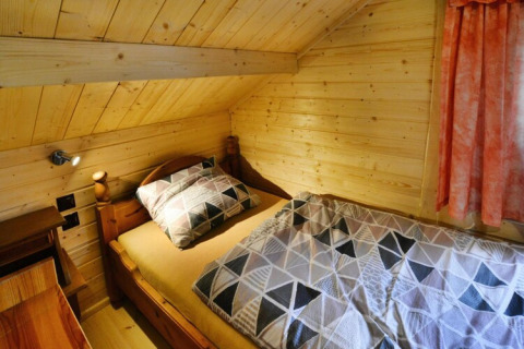 Gemütliches Schlafzimmer mit Holzwänden, Einzelbett und moderner Bettwäsche, orange Vorhänge am Fenster.