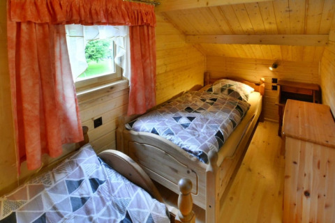 Gemütliches Schlafzimmer mit zwei Einzelbetten, Holzverkleidung, einem Fenster mit rosa Vorhängen.