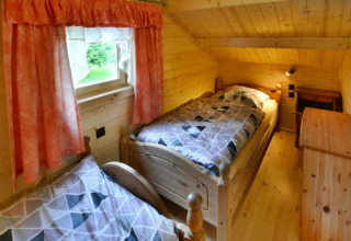 Gemütliches Schlafzimmer mit zwei Einzelbetten, Holzverkleidung, einem Fenster mit rosa Vorhängen.