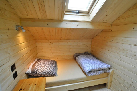 Gemütliches Schlafzimmer aus Holz mit Dachfenster und Einzelbett mit gemusterten Decken in einer Lodge.