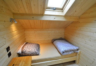 Gemütliches Schlafzimmer aus Holz mit Dachfenster und Einzelbett mit gemusterten Decken in einer Lodge.