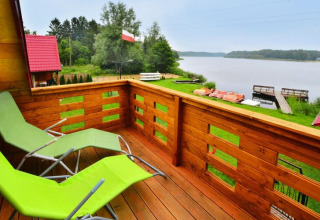 Blick von einem Balkon mit grünen Liegestühlen auf einen See und Boote, Domek letniskowy PATRYK Ostrowiec Slawienski.