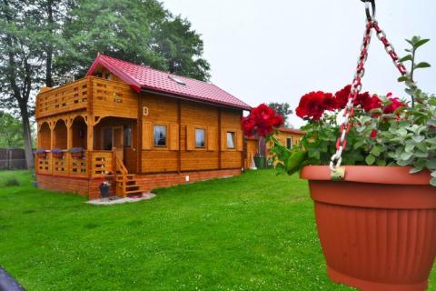 Holzhütte mit rotem Dach und Balkon, umgeben von grünem Rasen und Blumentopf in Domek letniskowy PATRYK.