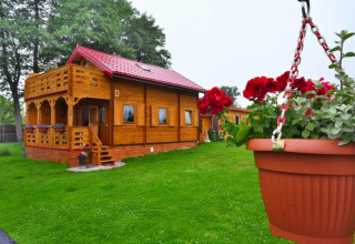 Holzhütte mit rotem Dach und Balkon, umgeben von grünem Rasen und Blumentopf in Domek letniskowy PATRYK.