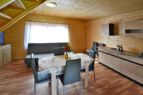 Interieur van een houten lodge met eettafel, vier stoelen, bank en kitchenette in Jarosławiec.