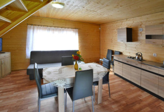 Interieur van een houten lodge met eettafel, vier stoelen, bank en kitchenette in Jarosławiec.