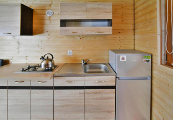 Compact kitchenette featuring wooden panels, stove, kettle, sink, and fridge at Jarosławiec lodge in Denmark.