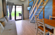 Interno di un lodge accogliente con mobili in legno, divano, scale per il soppalco e vista sul verde.