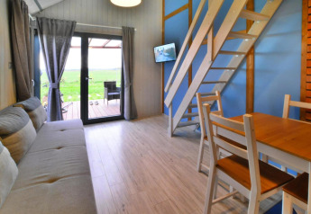 Interno di un lodge accogliente con mobili in legno, divano, scale per il soppalco e vista sul verde.