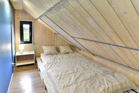 Soveværelse i Domki wakacyjne Jezierzany-lodgen med skrå loft, dobbeltseng og natbord.