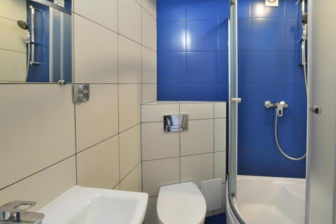 Moderne badeværelse med blå og hvide fliser, brusekabine, toilet og håndvask i Domki wakacyjne Jezierzany.