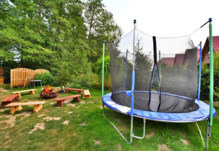 Buitenruimte bij Domek 5-osobowy Jarosławiec met trampoline, vuurplaats en houten bankjes tussen het groen.