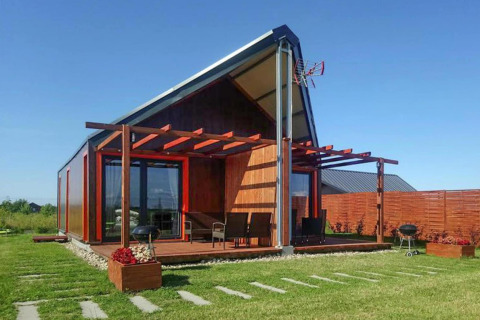 Moderne feriebolig ved Domki wakacyjne Jezierzany med træterrasse, grill og grøn have under blå himmel.