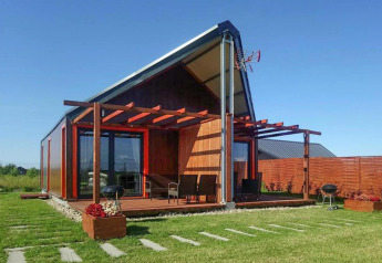 Modernes Ferienhaus bei Domki wakacyjne Jezierzany mit Holzterrasse, Rasenfläche und Gartenmöbeln.
