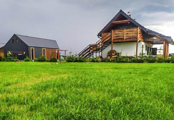 Ein Ferienhaus namens Domki wakacyjne Jezierzany in Dänemark, aufgenommen von einer großen Wiese bei bewölktem Himmel.