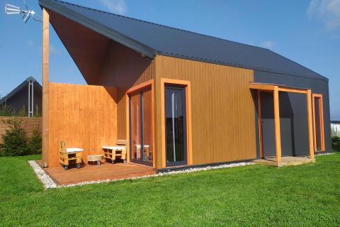 Moderne træhytte med stor terrasse og unikt tagdesign i grønne omgivelser ved Domki wakacyjne Jezierzany.