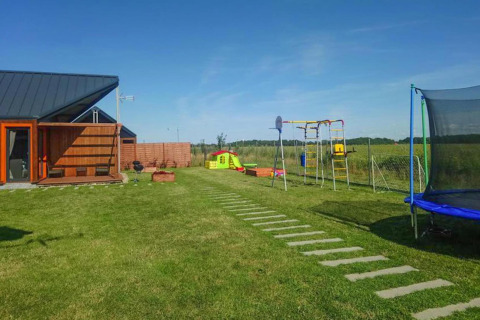 Udendørs legeplads og lodge ved Domki wakacyjne Jezierzany, med græsplæne, gyngestativ og trampolin.