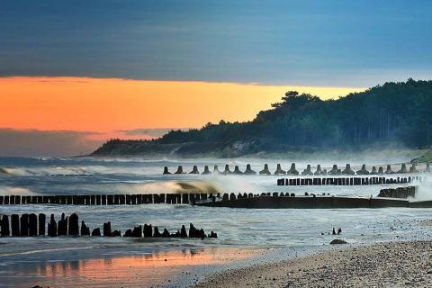 Kustlandschap bij zonsondergang met golven en houten palen nabij Domek 5-osobowy Jarosławiec lodge.