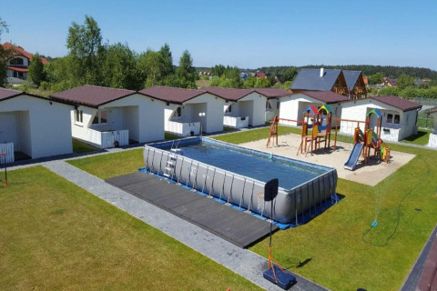Feriehytter med gynger, legeområde og en stor oppustelig swimmingpool på grønne græsarealer.