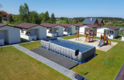 Feriehytter med gynger, legeområde og en stor oppustelig swimmingpool på grønne græsarealer.