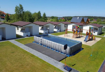 Chalets de vacances avec aire de jeux, balançoires et grande piscine gonflable sur pelouse verte.