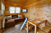Cozy wooden lodge interior at Domki wakacyjne Przewłoka featuring sofa, dining table, and TV.