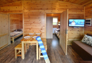 Gezellige houten lodge met eettafel, sofa, televisie en twee slaapkamers in Domki wakacyjne Przewłoka.