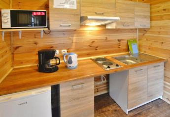 Pequeña cocina de madera con microondas, cafetera, hervidor, placa doble, fregadero y nevera.