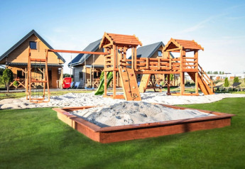 Playground with swings, slide, and sandbox in front of cozy wooden lodges at Ustecka Osada 45m2 in Denmark.