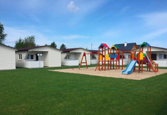 Bunter Spielplatz mit Rutschen und Holzhäusern im Hintergrund, gelegen auf einer grünen Wiese.