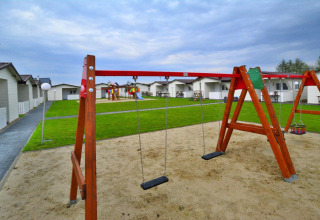 Speelplein met schommels en zandbak voor moderne lodges bij Domki wakacyjne Przewłoka in Denemarken.