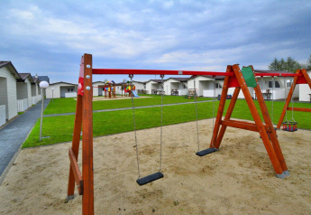 Parco giochi con altalene e sabbiera davanti a lodge moderni presso Domki wakacyjne Przewłoka in Danimarca.