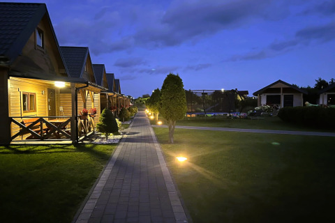 Avondzicht op Ustecka Osada 45m2 lodge in Denemarken met houten huisjes, verlichte paden en gras.