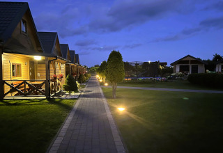 Avondzicht op Ustecka Osada 45m2 lodge in Denemarken met houten huisjes, verlichte paden en gras.